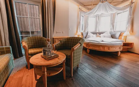 Himmelreich Gemütliches Hotelzimmer mit rundem Bett, Holzfußboden und Sitzbereich mit zwei Sesseln